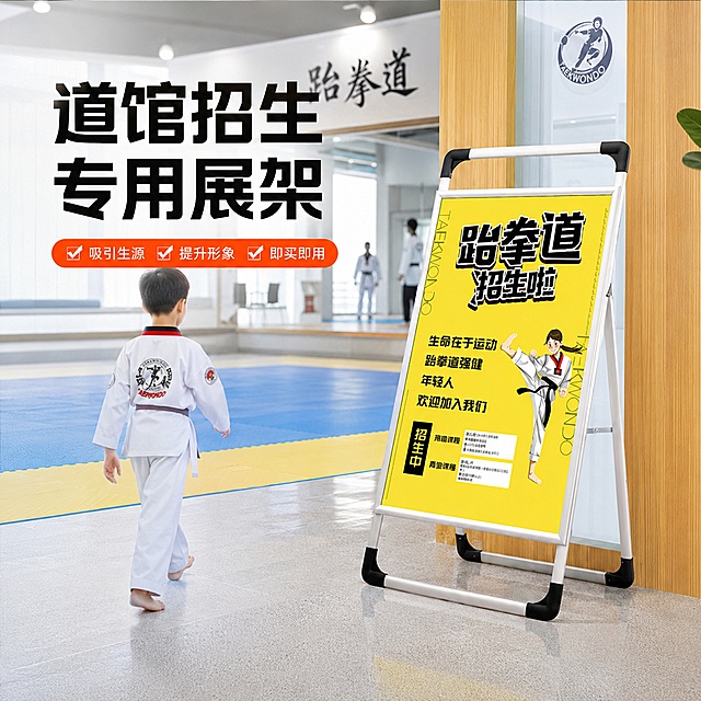 淘宝天猫电商主图，1:1正方形，跆拳道招生海报展架使用场景主图，展架放置在跆拳道馆入口处，旁边有穿着跆拳道服的学员走过，背景是明亮的道馆环境，地垫、镜子等元素隐约可见，营造真实使用场景，画面有商品名称文字"道馆招生专用展架"，卖点文字"吸引生源 提升形象 即买即用"，整体氛围活力专业，场景化展示，真实感强