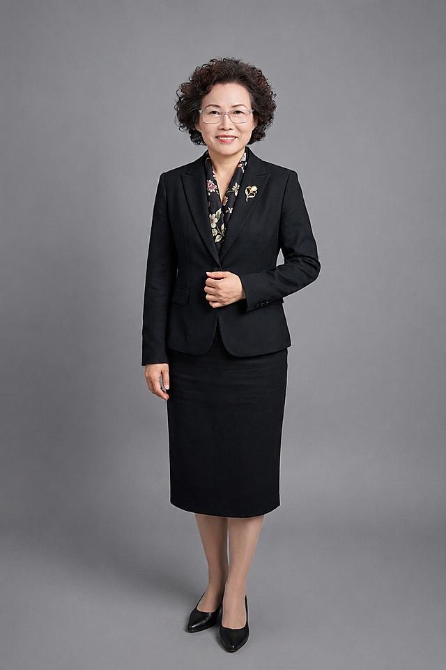 参考图中，把第二张图https://gdesign-dam-hz.dancf.com/37186379784246353/9b3a5663b2174e23b808a07481157e20.png的人脸替换到第一张图https://dify-grsai.dancf.com/images/5888ad9fcc424f41b1fa0e94b2f721c8.png的身体上，严格保留原图人物的五官、年龄、短卷发和透明方框眼镜特征，保留第一张图的黑色西装、黑色印花丝巾、金色胸针、人物姿势和灰色背景，生成一张自然协调的中长款全身职业形象照，融合自然，不要有拼接痕迹