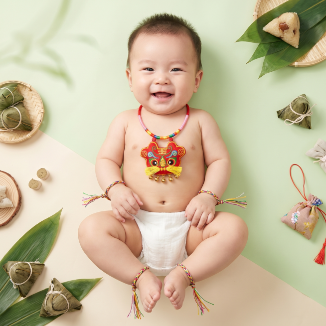 商品精修，生成1张百天婴儿佩戴的端午节挂件主图，1:1比例，端午节气氛清爽底色，婴儿脖子上戴着图1的项圈香包，手腕和脚腕上戴着图2的五彩绳预览效果