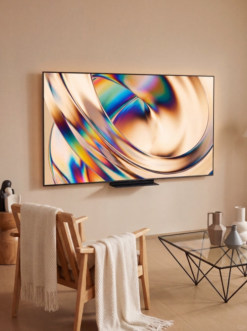 黑色平板液晶电视，超窄边框，黑色底座，屏幕显示彩色动态画面。保持物理结构不变，严禁扭曲拉伸改变产品形态。北欧风客厅场景，暖调浅米色奶油色调，搭配原木单人扶手椅和黑色金属框架玻璃茶几。柔和漫射柔光，【产预览效果