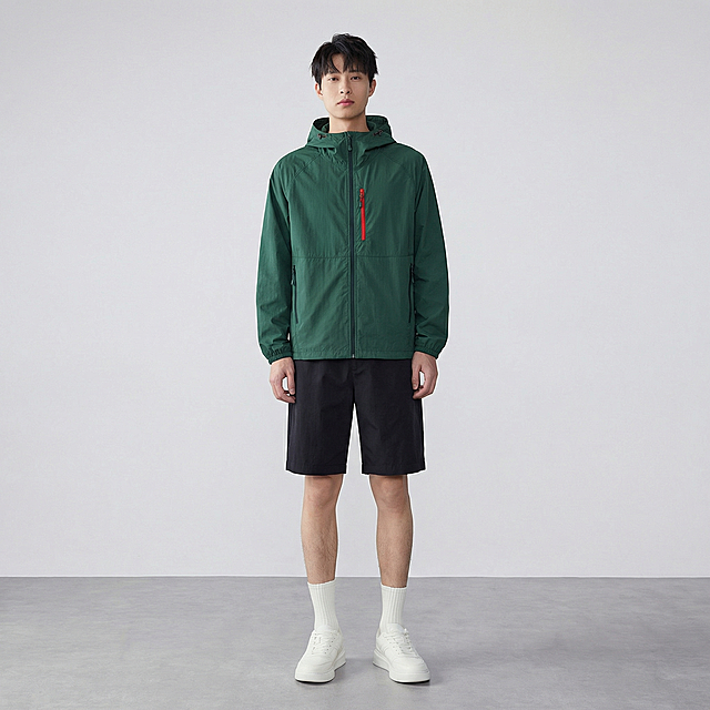 将图片1中的墨绿色带帽连帽外套替换到图片2的模特身上，要求衣服完全贴合模特身形，无违和感，保留衣服原有版型、墨绿色颜色、红色拉链细节、黑色口袋拉链细节，无变形，无颜色偏差，保留所有细节。背景保留图片2的灰色地面与浅白色背景，光线自然自然，写实风格，8k，高细节，对焦清晰，无变形