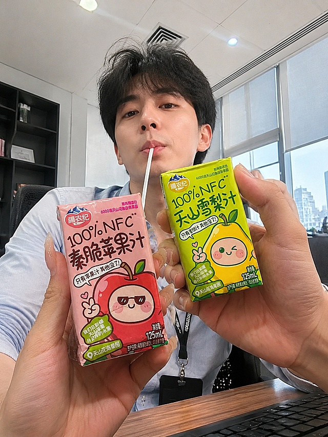 添加中国年轻帅哥低角度仰视拍摄喝果汁的办公室背景，保留产品形状、颜色、包装文字和手持姿势完全不变，果汁饮料完整保留所有文字与图案，帅哥自然入镜，产品仍在画面中心，自然融入场景光影，风格写实，严格锁定宽高比为3:4