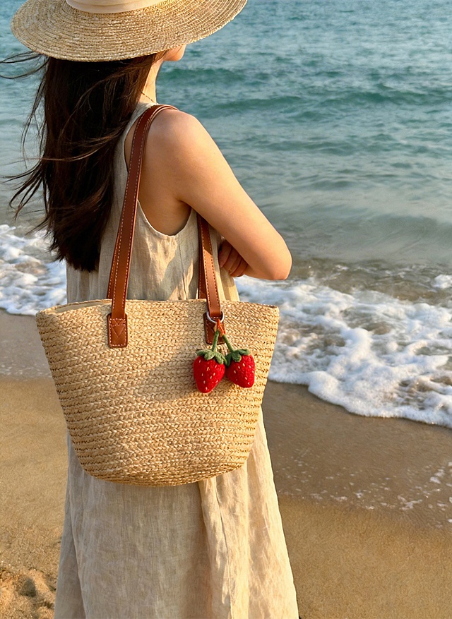 清新自然风，编织包搭配刺绣草莓挂饰，质朴与柔美交织，实景海边氛围感拉满，夏日舒适惬意。
