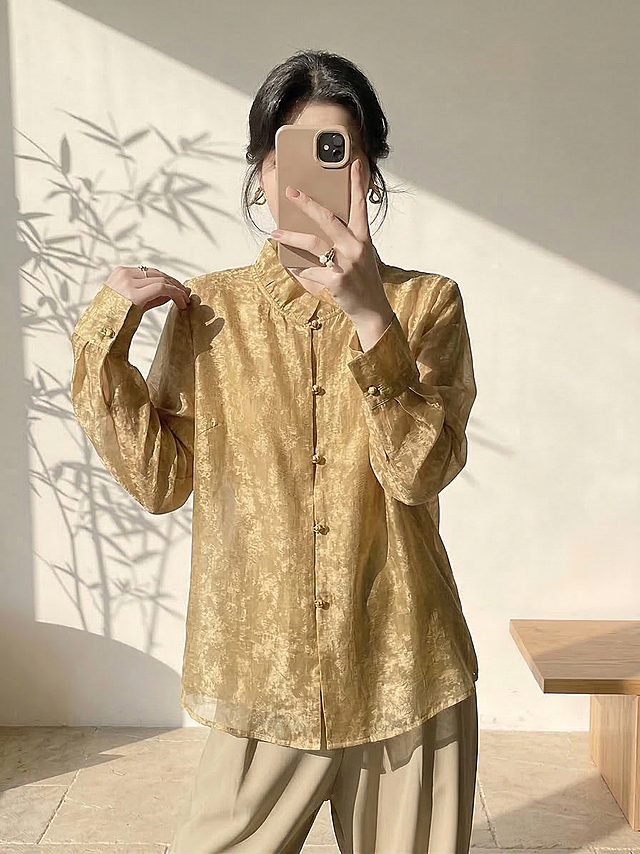 保持人物姿势、身材比例、脸型发型和背景不变，仅将人物身上的白色衬衫替换为图片中的芥末金色提花新中式衬衫，保留这件金色衬衫的所有细节：木耳边立领、金色盘扣、金丝提花纹理、通透的纱质面料和版型，适配人物身体自然呈现穿着效果，光影和风格与原图保持一致，服装自然贴合身体，不改变人物整体结构。负向提示词：服装变形、细节丢失、颜色不对、纹理错误、比例失调、人物扭曲、水印、文字