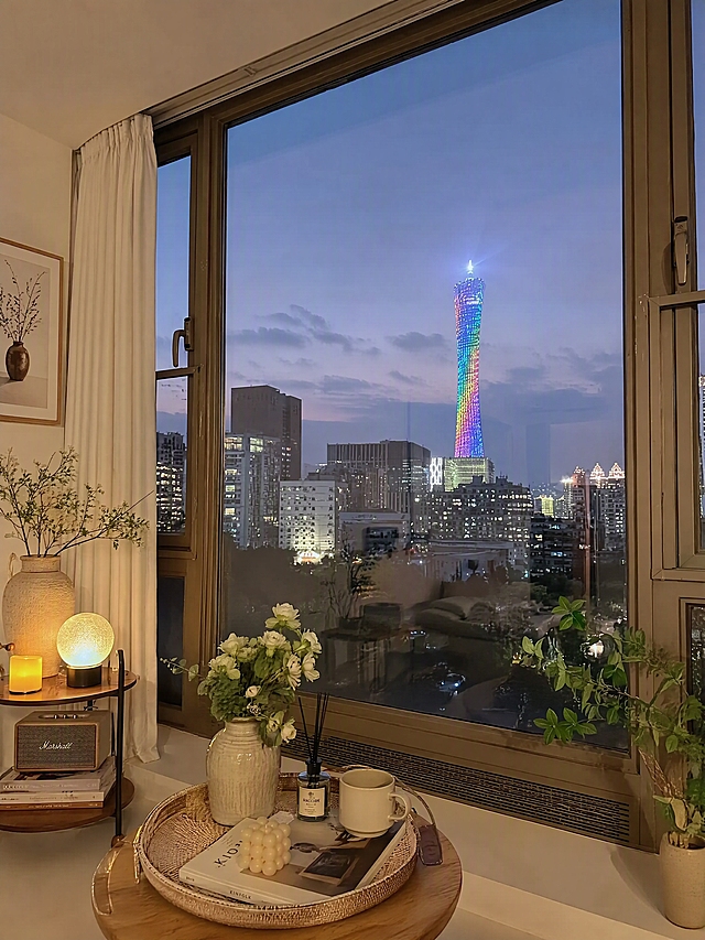 基于原图进行重绘，保持广州塔夜景窗边整体布局结构不变，整体色调明亮通透不压暗，避免阴沉发灰，滤镜不过黄，画面真实自然协调。增强生活感和氛围感，增加更多摆件和装饰物品，如绿植、装饰摆件、书籍、香薰、水杯、托盘、窗帘装饰、挂画、小边几等，画面物品丰富有层次，营造小红书酒店民宿氛围感。4K高清画质，细节精致，独立出图不拼图。第二版，物品摆放和细节与第一版不同