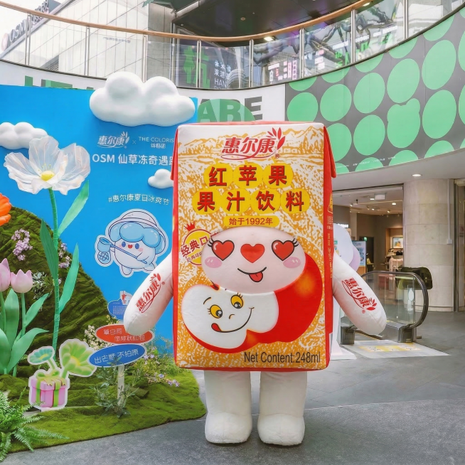 将图中的惠尔康优の冻玩偶服装替换为惠尔康红苹果果汁饮料包装形象，保留玩偶原本的卡通表情，整体画质清晰，色调平衡自然预览效果