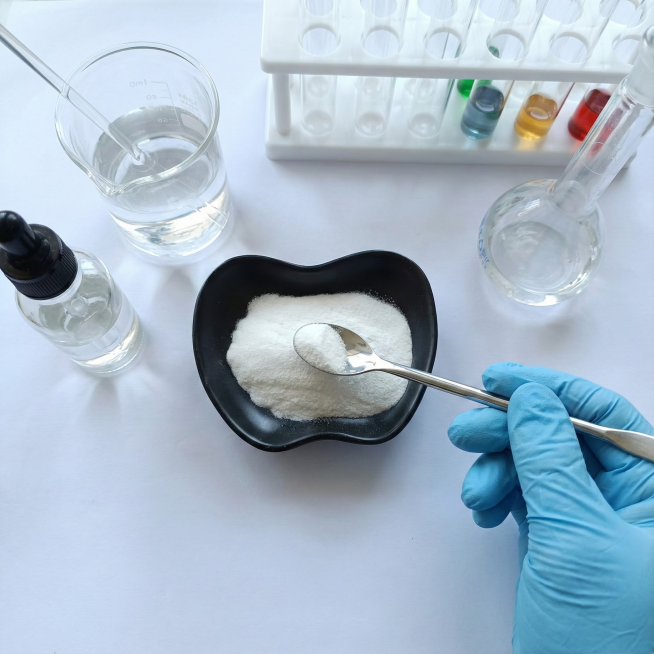 帮我为这个产品，生成周围有一些化学器材，然后一只戴着浅蓝色硅胶手套的收拿着勺子准备去勺他，视角保持不变预览效果