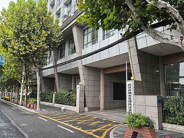 去掉画面中停放在建筑入口处的黑色轿车，将其所在区域自然修复为人行道地面和建筑入口背景，补全被遮挡的地砖、台阶和墙面，保持周围树木、建筑、标牌和其他元素完全不变，画面自然无痕迹
