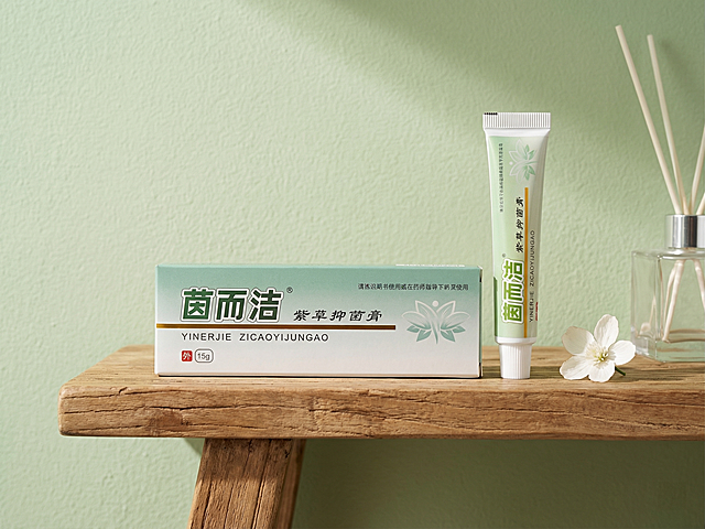 保持茵而洁紫草抑菌膏包装盒和软管的所有文字、Logo、外形完全不变，产品放置在原木浴室洗手台搁架上，旁边搭配一朵素雅的白色小花和透明玻璃香薰瓶，背景是干净的浅绿调硅藻泥墙面，柔和的自然光从侧面照入，营造清新自然、干净私密的女性护理氛围，简约高级风格，4K超清画质。变形,扭曲,悬空,比例失调,杂乱,死黑阴影,硬光,高对比度,西方面孔