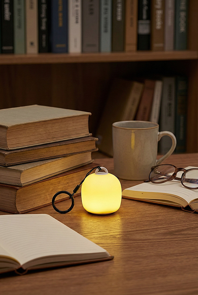 帮我生成图片：参考图中的捏捏灯放置在书房的桌子上，桌子有书的场景，捏捏灯发着光