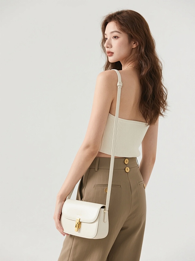 时尚产品摄影，女性模特，侧后方视角，柔和的自然光，极简主义白色背景，米白色针织抹胸上衣，卡其色高腰直筒长裤，金色纽扣细节，光滑的象牙白色皮质包包，金色金属配件，精致的缝线工艺，模特自然垂放的手臂，优雅的站姿，清晰的产品细节，柔和的阴影，高清晰度，柔和的肤色，棕色长卷发，简约现代风格，专业的商业摄影，突出包包的质感和设计，整体色调温暖和谐，干净利落的构图，无logo和文字。