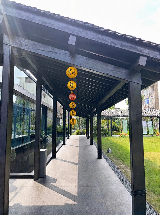 重新调整灯笼：6个中秋节灯笼必须严格对齐在连廊走道的正中心垂直线上，沿连廊纵深方向排成笔直的一条直线，所有灯笼的中心点都在连廊的中轴线上，左右完全对称。灯笼尺寸进一步缩小，最近处的灯笼直径约30-35厘米，适配2.5米层高的连廊，灯笼底部距离地面约2.2米。严格遵循近大远小透视，从近到远均匀递减变小，间距均匀。灯笼悬挂在顶部横梁正下方，红绳垂直向下。保持原图所有建筑、庭院、光线、环境元素完全不变，真实感强，超写实，高清摄影质感