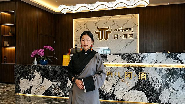 参考图1人物五官特征，将图片修改为16:9比例，保留阿酒店前台背景，写实清晰，保持人物和环境自然融合