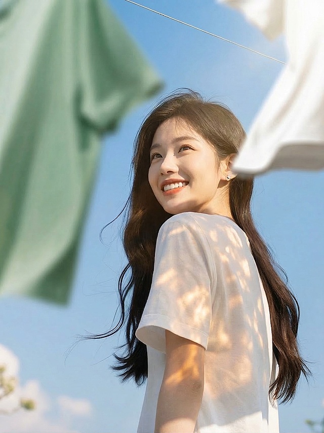 去掉图片左侧和底部的文字，调整女生头部姿态让头抬高一些，修改面部表情让笑容更灿烂，在背景增加阳光光影效果，保留人物穿着白色短袖、晾晒的衣物和蓝天背景，其余保持不变