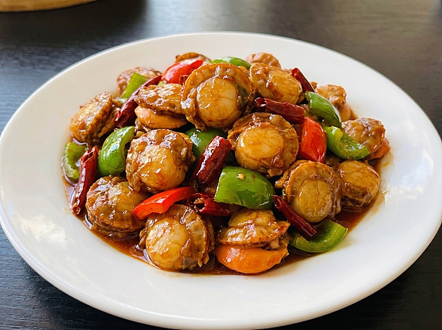 参考图风格生成小炒扇贝肉，盛放在圆形白盘子中，45度拍摄角度，真实菜品摄影风格，扇贝肉裹着红亮酱汁，搭配青红椒，诱人食欲