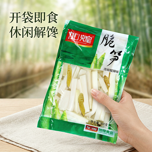 垫图为用户提供的加煌脆笋泡椒酸辣味商品图，生成第四张泡椒脆笋电商主图，模拟手持包装袋展示的生活场景，一只手自然拿着大袋泡椒笋，背景是干净的野餐布，搭配浅景深的竹林背景，营造休闲野餐的食用场景，代入感强，整体风格清新自然，和前面主图风格统一。文案"开袋即食 休闲解馋"，文字悬浮在画面左上角留白处，不遮挡产品和手部，背景铺满无边框，光影自然通透。