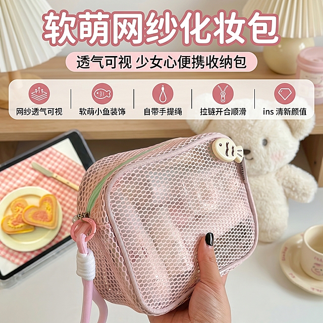 严格还原网纱化妆包产品图，包括包装设计、颜色、LOGO 位置、文字内容、图案元素等所有细节，尺寸比例保持 1:1。整体采用软萌少女 ins 杂志风，主色调为浅粉色 (#FADADD) 与白色 (#FFFFFF)，搭配浅绿色、米黄色作为辅助色。画面中心为手持化妆包的特写，清晰展示粉色网纱材质、小鱼装饰、手提绳与拉链细节，背景搭配可爱玩偶与少女风桌面道具；顶部设置大号圆润无衬线主标题 “软萌网纱化妆包”，副标题为 “透气可视 少女心便携收纳包”，下方用分区文字标注核心卖点：“网纱透气可视、软萌小鱼装饰、自带手提绳、拉链开合顺滑、ins 清新颜值”，整体排版活泼清爽，像少女杂志一样层次分明，高清细腻，光影柔和，风格统一无割裂感，30 秒内可快速抓住用户注意力，突出产品的颜值与实用性。负面提示词：模糊画质、低分辨率、产品细节失真、颜色偏差、风格割裂、排版杂乱、画面拥挤、网纱材质纹理模糊、小鱼装饰变形、手提绳断裂、拉链细节丢失、文字乱码、比例失调、与原产品不符、画面有多余元素、光影杂乱、有水印、不符合电商主图规范、高级感缺失、卖点信息不清晰、背景过于花哨