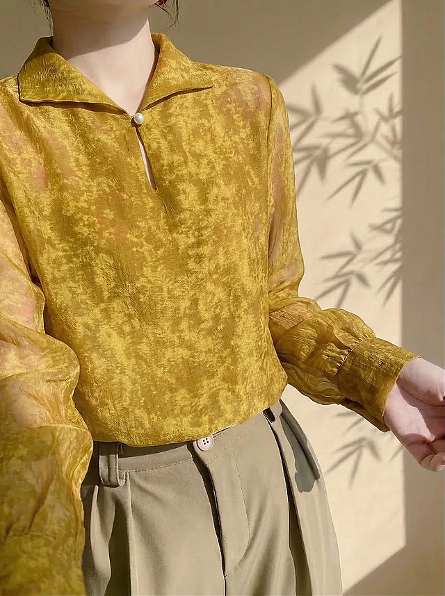 保持人物和姿态不变，将原来的白色衬衫替换成上传图片中的这件芥末黄扎染纹理长袖衬衫，保留这件新衬衫的芥末黄色、扎染花纹、翻领珍珠扣设计、透视感和面料纹理，适配人物穿着的版型和褶皱。背景保持原有的暖色系新中式极简风氛围不变。

负向提示词：衣服变形，颜色扭曲，花纹丢失，版型不对，人物脸部变形，水印，文字，多余元素