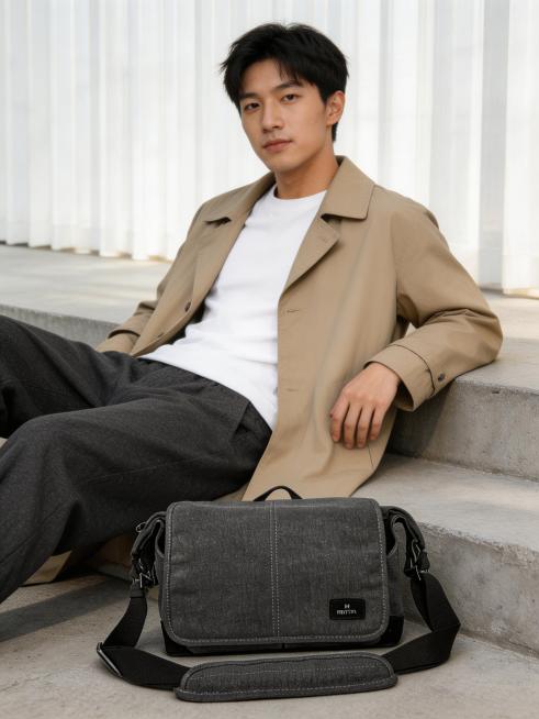 简约风户外城市商业人像摄影，电商背包产品广告场景，日韩清新画报风格，自然日常的松弛感穿搭氛围。年轻亚裔男生，卡其色风衣+白色内搭T恤+阔腿裤，韩系通勤休闲穿搭。男生斜坐水泥台阶上，主体单肩包放置在人物预览效果