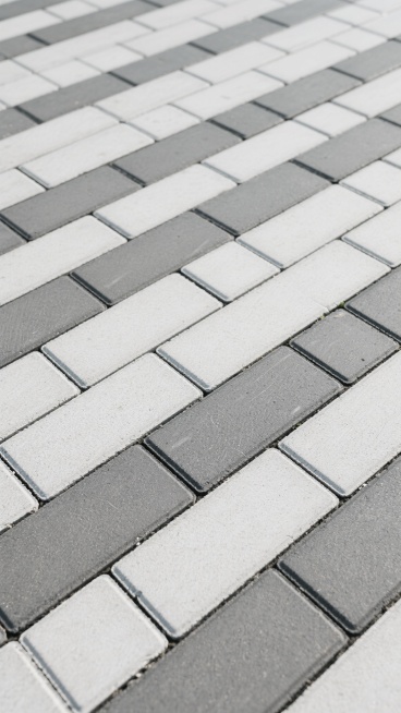 浅灰色与中灰色相间的长方形混凝土铺路砖，以纵向四列交错排列的方式紧密铺就，砖块表面呈现出细腻均匀的磨砂质感，砖缝为深灰色细线且宽度一致，整体构成无缝平铺的地面纹理，光线均匀柔和，营造出简洁、规整、略带工业风的朴素氛围。预览效果