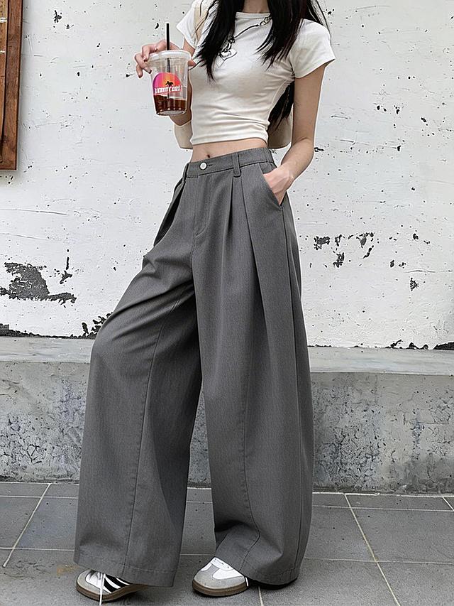 将图二的灰色阔腿西装裤替换到图一模特的下半身，保持图一模特的姿势、白色短袖上衣、手中的饮品、背景墙面地面、鞋子都完全不变，裤子贴合模特身材，光影自然，与整体画面协调统一