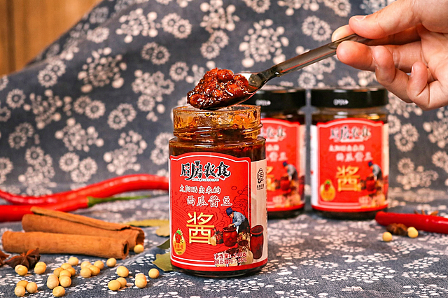 精修这张美食照片，处理成专业商业摄影风格：重点增强酱料表面的油润光泽感，使其晶莹剔透；提高色彩饱和度和对比度，让酱色更加浓郁诱人；强化微距下的纹理细节，突出酱料的浓稠度和颗粒感；添加一层柔和的暖色调美食灯光，让整体画面更具食欲。保持原有构图和产品内容不变。