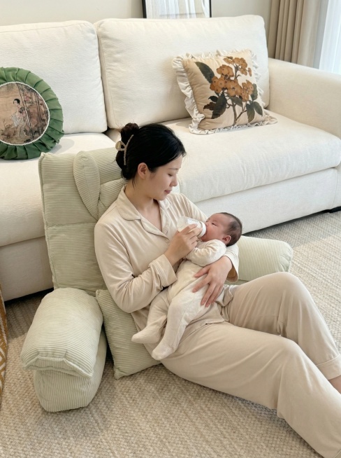 帮我生成几张图片，女性穿着睡衣靠着图片里的大靠枕，抱着婴儿用奶瓶喂奶。几张图片人物保持一致，衣服都要一样，其他不用改变。小枕头是腰靠枕不是坐垫预览效果