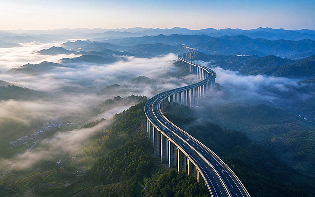 参考图片风格，重新生成清晨山间高速公路高架桥的画面，保留云雾缭绕山林的氛围感和写实风景摄影风格