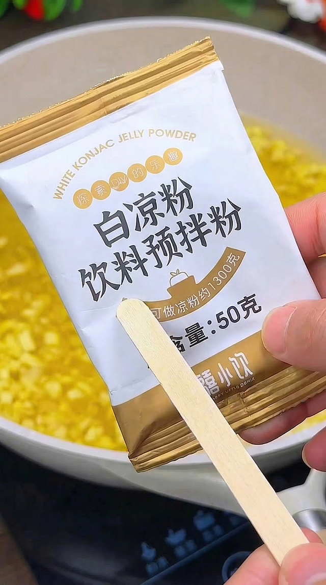 去除图片底部的时间条和预览栏以及下方文字，仅保留核心内容：手持白凉粉饮料预拌粉包装袋展示，背景是熬煮菠萝丁的不沾炒锅，保持9:16比例，真实写实风格，其他内容不变