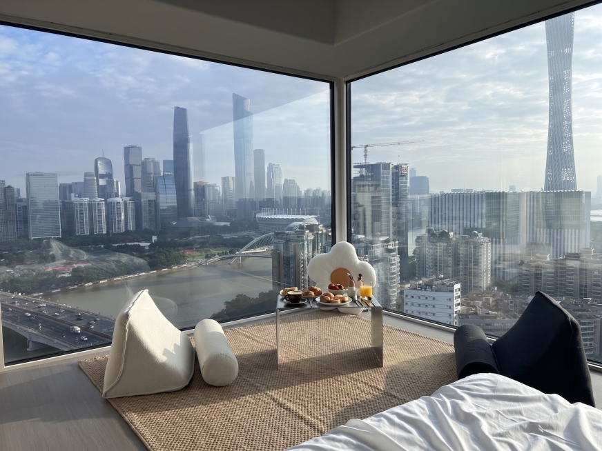 在窗前小桌子上摆放一份早餐，在地板上铺设一个垫子，保持江景城市景观和房间整体布局风格不变，真实自然预览效果