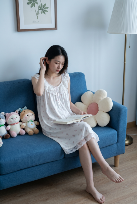 基于参考图中的衣服，生成一张生活照：一位年轻中国女性，身材纤细，身穿这件白色带粉色碎花的蕾丝花边睡裙，保持衣服面料质感，重点保留衣服的花边细节，她坐在蓝色沙发上，旁边放着花朵形状的抱枕，她低头看书，一预览效果