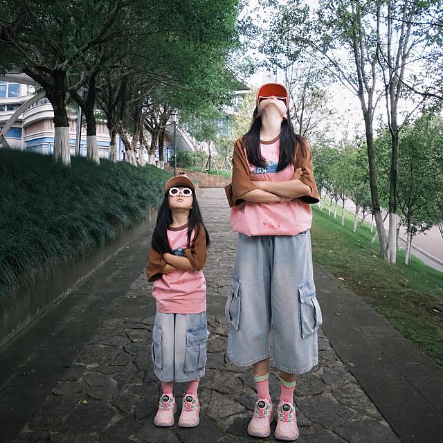 将图中两个人脚上的黑色洞洞鞋替换为图一的粉色儿童运动鞋（带有旋转纽扣、粉色鞋带、蓝绿色装饰、鞋底为淡粉色），鞋子的角度和透视要与脚部姿态匹配，自然贴合脚部，其余画面内容保持不变，包括人物、服装、背景环境、光线、色调等全部保持原样