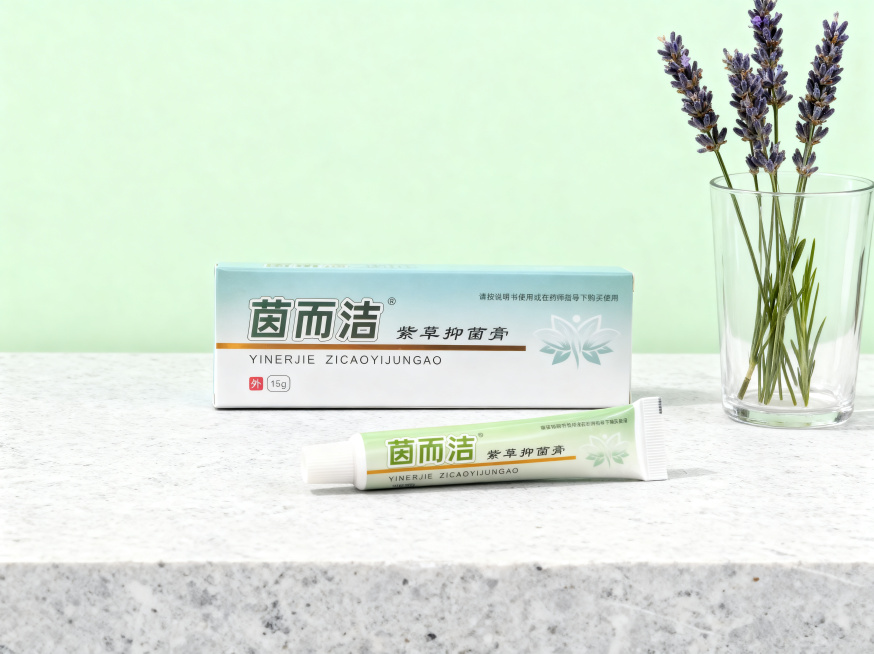 保持茵而洁紫草抑菌膏包装盒和软管的所有文字、Logo、外形完全不变，将产品摆放在干净的浅灰色石材台面上，旁边放置一只透明玻璃杯中插着几支天然薰衣草，背景是哑光浅豆绿色墙面，柔和均匀的室内自然光，营造干预览效果