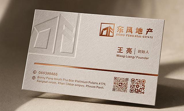 将参考图中的名片做成棉卡材质烫红金的高端效果图，正面左上角的灰色logo做压凹效果，整体画面有空间感、高级质感，光影细腻，棉卡纸纹理清晰，烫红金文字和logo呈现金属光泽与凹凸立体感，压凹logo有明显凹陷肌理，名片以优雅角度摆放，背景简洁高级，突出名片的高端品质