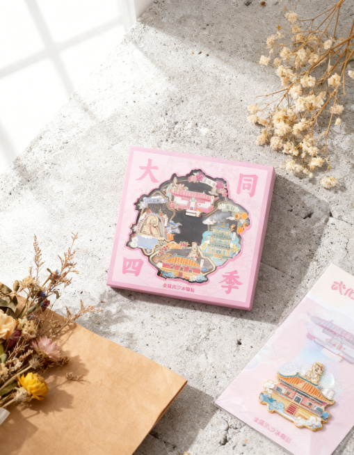 产品主体为大同四季金属流沙冰箱贴文创产品，保持产品主体物理结构不变，保持所有文字和Logo原样，强制保留产品完整。更换全新场景为浅灰色水泥台面，旁边搭配干花牛皮纸包装和同系列文创小卡片，营造真实博主拆预览效果