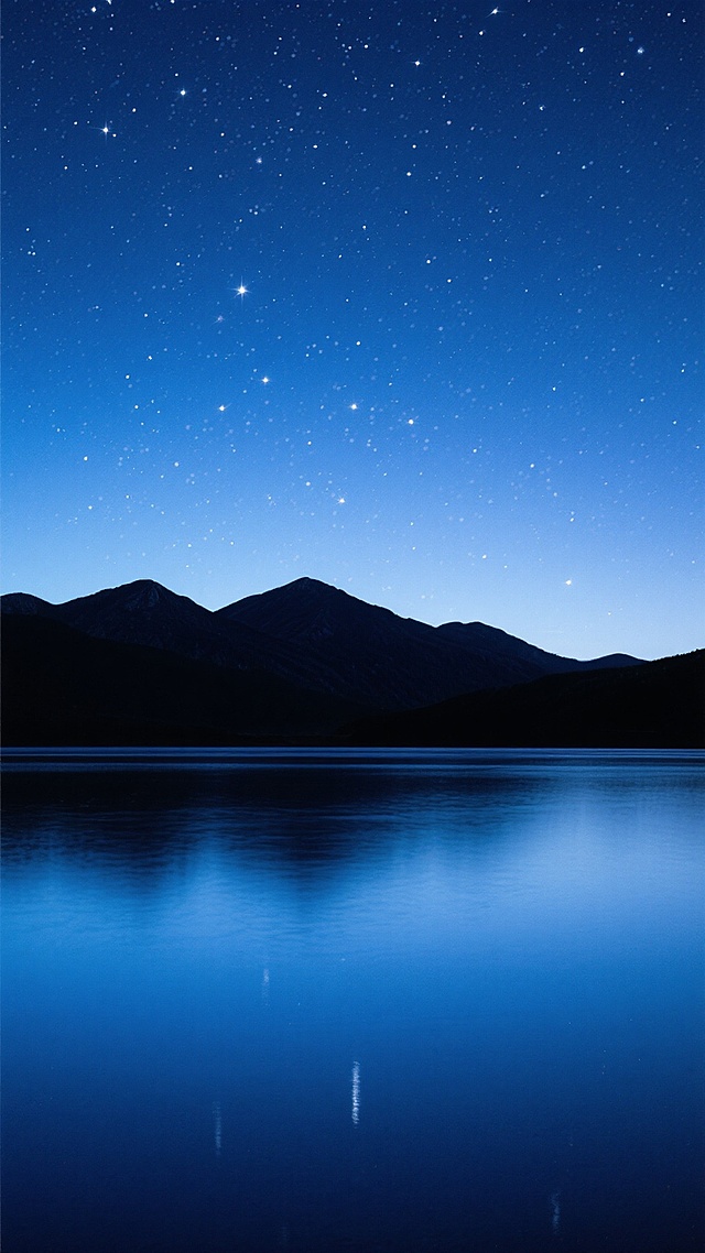 深邃的夜空，从上到下呈现由墨蓝到浅蓝的渐变色彩，布满无数闪烁的白色星星，星星分布自然且密集，夜空下是轮廓清晰的深色山脉剪影，山脉底部是平静的深蓝色水面，水面倒映着夜空的颜色，整体画面宁静、悠远，营造出静谧而浩瀚的氛围，竖构图。