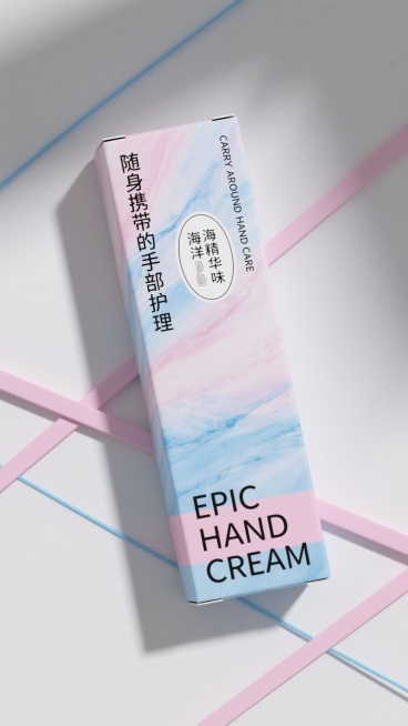 白色背景上，一个斜放的长方形产品包装盒，盒面覆盖着柔和的粉蓝色和浅蓝色大理石纹理渐变图案，顶部左侧有竖排黑色中文文字“随身携带的手部护理”，右侧有竖排黑色英文“CARRY AROUND HAND CARE”，中间偏上位置有一个椭圆形白色标签，内部是黑色中文“海洋精华味”，底部有一条横向的粉蓝色宽幅区域，内部用黑色大写英文字母写着“EPIC HAND CREAM”，背景中有数根交叉的粉蓝色细长线……预览效果