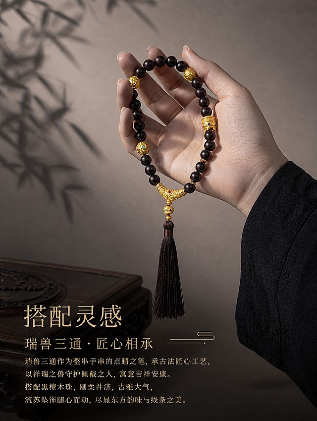 古法黄金瑞兽三通搭配场景详情页，暗调黑金国风风格。画面展示瑞兽三通搭配在黑色木质念珠手持上的整体效果，带流苏坠饰。浅灰褐色质感背景，柔和侧光，左侧有植物叶影投影。下方文字搭配灵感标题和说明文字，讲述三通与手串的搭配效果。古典宋体字，浅金色文字，横向排版。竖版3:4比例，4K高清文玩珠宝摄影。