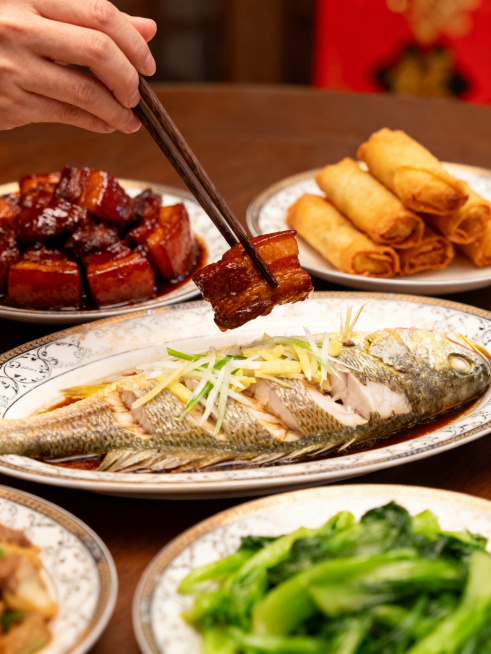 特写年夜饭餐桌，多种菜肴分区摆放：油亮的红烧肉、鲜嫩的清蒸鱼（带葱丝姜丝）、金黄酥脆的炸春卷、翠绿的时蔬，每种菜色差异明显，用精致餐盘盛放，一只筷子正从红烧肉转向清蒸鱼，画面聚焦“换菜”动作，背景虚化预览效果