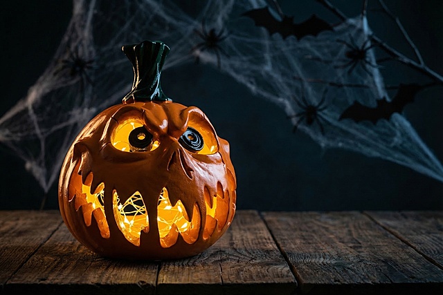 保持南瓜主体物理结构不变，保留所有造型细节，将南瓜放置在深色木质桌面上，调整南瓜为自然的其他展示角度，在南瓜镂空内部塞入暖光黄色灯串，营造真实充满氛围感的万圣节场景，经典侧逆光勾勒轮廓，柔光补光照亮暗部，深暗冷色调背景，带有万圣节蜘蛛、蝙蝠等节日装饰元素，整体画面有前中后景层次，商业摄影质感，真实写实风格，氛围恐怖诡谲，保持产品主体清晰，保留南瓜原有造型和橙色绿色配色不变
