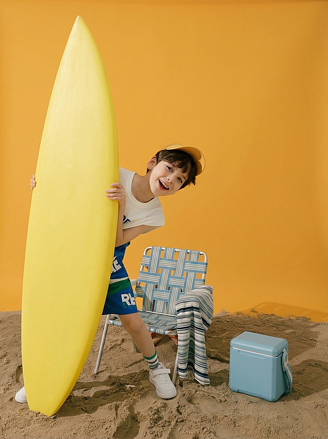 清新夏日海滩风，轻拟物与塑料质感结合，男孩手持冲浪板笑容灿烂，搭配浮雕感沙滩椅与冰桶，营造出清爽可爱、趣味十足的实景氛围。