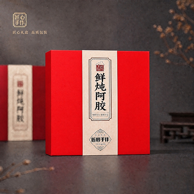 将画面中央的红色礼盒颜色调整为更鲜艳、更亮的正红色。礼盒从原来的暗红色/酒红色提升为明亮饱满的正红色，饱和度提高，亮度提升，呈现鲜艳亮丽的红色哑光质感。保持礼盒的结构、标签文字内容、背景环境、光影方向、投影、左侧虚化礼盒、干花装饰、左上角金色印章和文字全部不变。整体画面通透亮丽，红色鲜艳但不刺眼，质感依然高级。