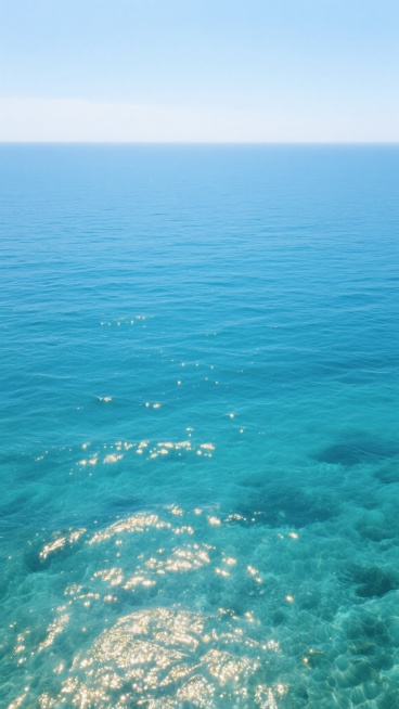 一张从高空俯瞰视角拍摄的海景照片，清澈透明的海水呈现出由浅至深的渐变蓝色，海面上荡漾着层层叠叠的水波，阳光洒在波光粼粼的海面上，泛起金色的光点，远处海天相接，天空呈现出纯净的浅蓝色，画面整体给人一种宁静、开阔、治愈的感觉，具有极高的信息传达效率，能在短时间内让观者感受到大海的壮美与平和。预览效果