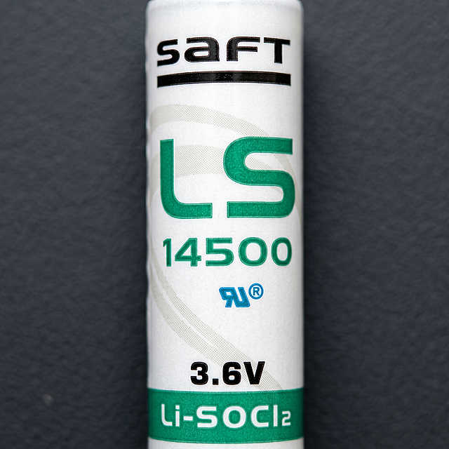 [主图-3] SAFT LS14500锂电池产品细节特写主图。
[氛围风格] 微距特写专业质感，突出产品工艺细节
[画质] 超高清商业摄影，细节纹理清晰锐利，材质真实可信
[元素] 对锂电池产品的标签印刷区域进行微距特写，展示清晰的品牌字样、型号标识和参数印刷细节，保持产品原有颜色和文字信息绝对一致，精细呈现包装材质质感和印刷精度。背景使用深灰色纯色，简洁不抢主体，画面满屏无边框。
[光影] 侧光打光突出表面纹理，高光勾勒边缘，阴影自然，材质表现力强
[配色] 深灰色背景，保留产品原本白绿黑标识配色，对比清晰
[视角构图] 微距特写构图，标签区域充满画面核心，景深较浅突出文字细节
[文字版式] 保留产品自身印刷文字信息，无需额外添加文案，细节清晰可辨
[比例分辨率] 1:1 比例，2k分辨率，文字清晰锐利，超高清
[负向提示词] 变形，水印，文字模糊，背景杂乱，色差，过度锐化