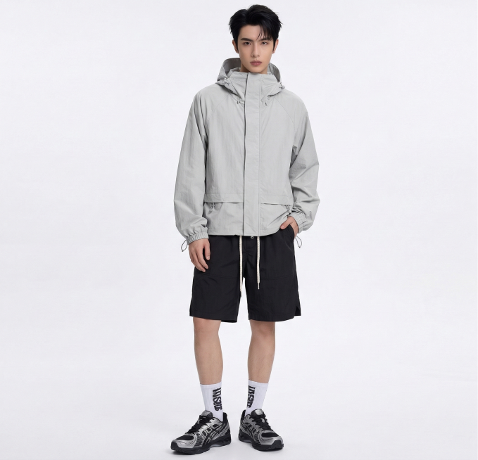 将图中模特的上衣替换为浅灰色连帽冲锋衣（图1款式），下装替换为带白色抽绳的黑色休闲短裤（图2款式），保持模特姿态和其他穿搭元素不变，服饰贴合身形自然预览效果