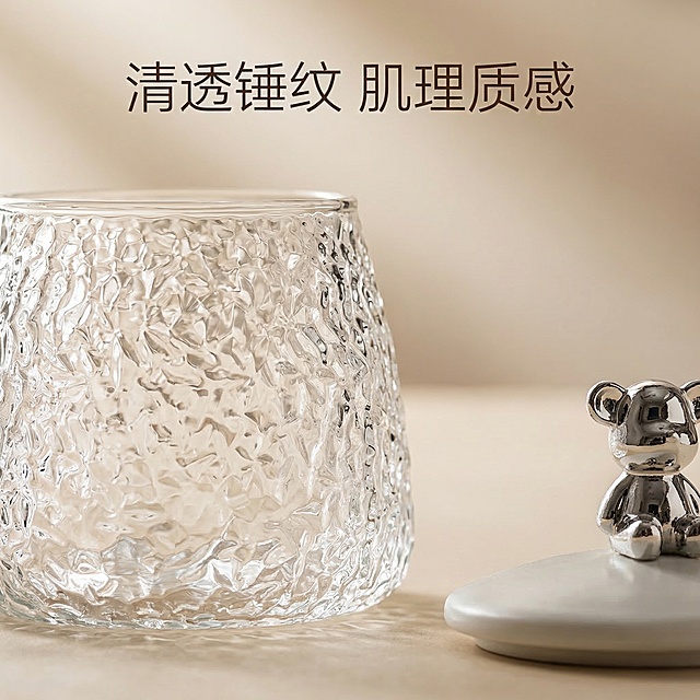 [垫图] https://gdesign-dam-hz.dancf.com/35887913630812296/bfc0a4ba67f64242b7a0d5fde7673b57.jpg
[主图主题] 玻璃杯细节质感展示主图
[氛围/风格] 舒适简约治愈风，侧逆光清透质感
[画面元素] 局部放大展示水杯锤纹玻璃肌理，侧逆光穿过透明杯身，清晰展现锤纹的立体凹凸纹理，小熊银色杯盖放置在水杯旁，背景为浅米色渐变，整体突出材质通透感与细节质感，画面干净聚焦于细节
[配色色系] 主色调：透明无色 浅米色；辅助色：银色 米白，整体干净清透配色
[视角构图] 微距特写，焦点清晰落在锤纹肌理上，背景虚化
[文字版式] 文案 "清透锤纹 肌理质感"，放在画面顶部居中位置，字体为细体无衬线，深棕色，排版简洁不遮挡细节，保持画面整体干净聚焦产品