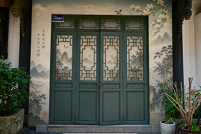 对该空铺进行包装设计：1.在所有大门玻璃窗内侧贴国风主题画面做遮挡美化；2.将门面周边左右上下的白墙区域整体用带国风画面的板子贴敷包装，打造完整适合打卡的点位，和墨绿色大门以及周边古建风格协调，真实实景效果图