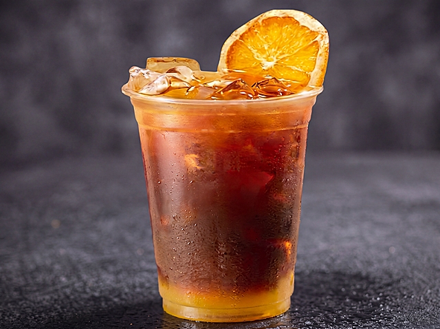 优化饮品图边缘与背景融合：1）柔化杯体边缘过渡，添加自然阴影与微反光，模拟真实置于深灰纹理台面上的效果；2）调整冷凝水珠与杯壁接触处的光影，使其与背景无缝衔接；3）保留橙片、冰块、液体分层等细节；4）确保无抠图痕迹，呈现真实拍摄质感；高清600*450