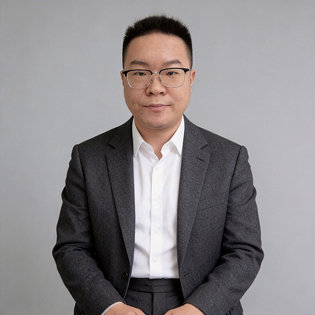 参考图中保留人物脸型、发型、年龄等特征，生成自然亲和不浮夸的商务形象照，适用于小红书和抖音头像。标准焦段50mm,f/4光圈，平视视角，人物占画面70%，居中构图，胸像照，头部与画面顶部保留适当空间，头肩比例协调，人物结构准确。身穿深灰精纺羊毛混纺西装外套，平驳领设计，面料呈细腻微微哑光质感，内搭白色高支精梳棉衬衫，下装深灰精纺羊毛混纺西裤，着装正式干练，专业稳重亲和，身形匀称，姿态端正，身体挺拔。呈自然站姿，双手轻放在身前，肢体放松且自信，佩戴黑框眼镜保留配饰，发梢微微修整，干练大气。中性灰简约纯色背景，呈现均匀柔和质感，背景光线均匀柔和，强化色彩对比的高级感，极简干净。画质超高分辨率，细节清晰，现代精致感风格，肤质精细化处理，眼神直视镜头，目光坚定澄澈，表情自然亲和，肤色均匀，哑光肤质，肤色均匀提亮，杰作，最佳画质，超高细节，写实摄影，近景人像，皮肤细腻通透，柔光，正面补光，画面干净清新，高清皮肤细节，面部光比1:1.5，4800K中性光，微微修饰脸型，肤质哑光细腻，面部雾面柔光，轻透裸肌感，真实毛孔纹理，不违和自然真实，严格保留脸型特征，画面比例1:1