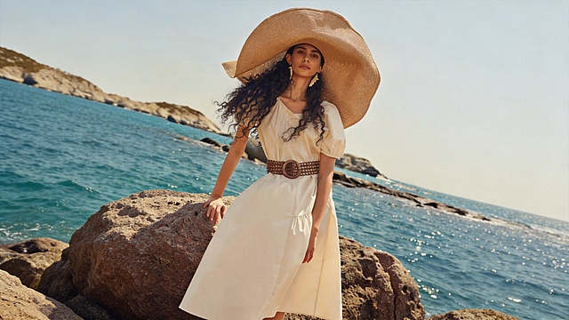 基于参考图生成16:9电商横幅，海边度假场景，模特穿着米白色连衣裙，佩戴大草帽和编织腰带，画面干净无任何文字文案，整体清新自然的高级时尚摄影风格